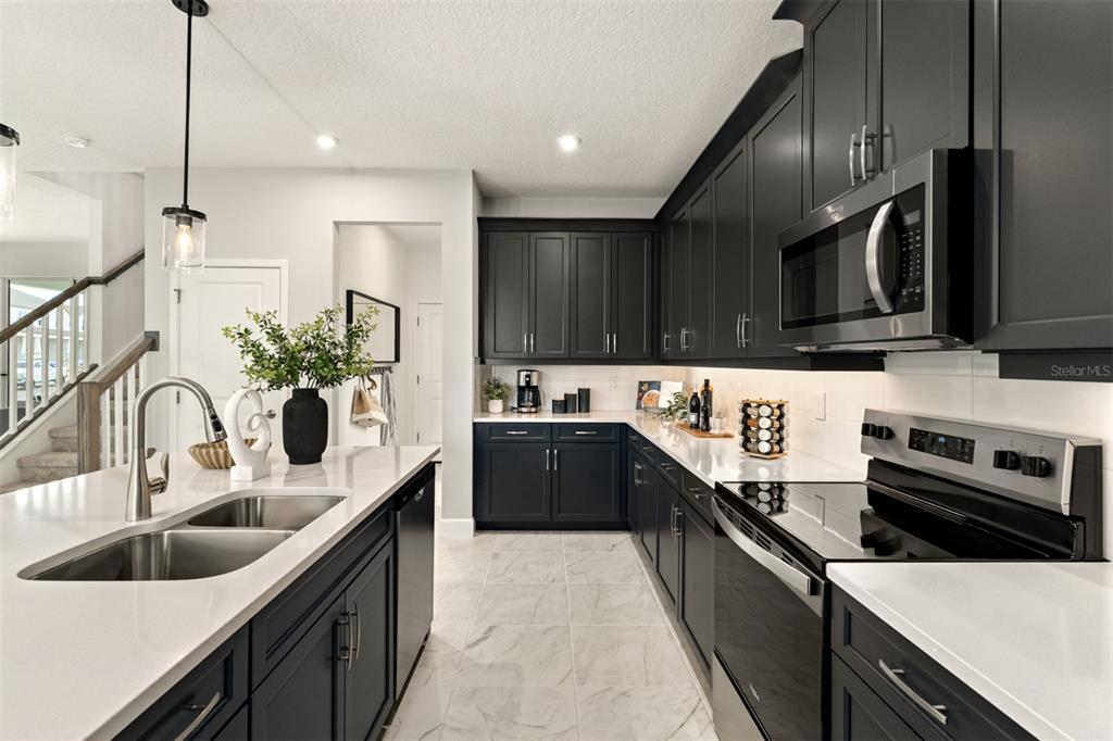 A modern kitchen features dark cabinetry, white countertops, stainless steel appliances, and tile flooring — 416 BANANA PEPPER WAY, GROVELAND, FL
