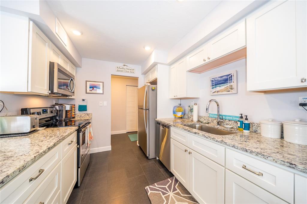 A galley kitchen features white cabinets, granite countertops, stainless steel appliances, and dark tile flooring — 707 S GULFSTREAM AVENUE UNIT 602, SARASOTA, FL