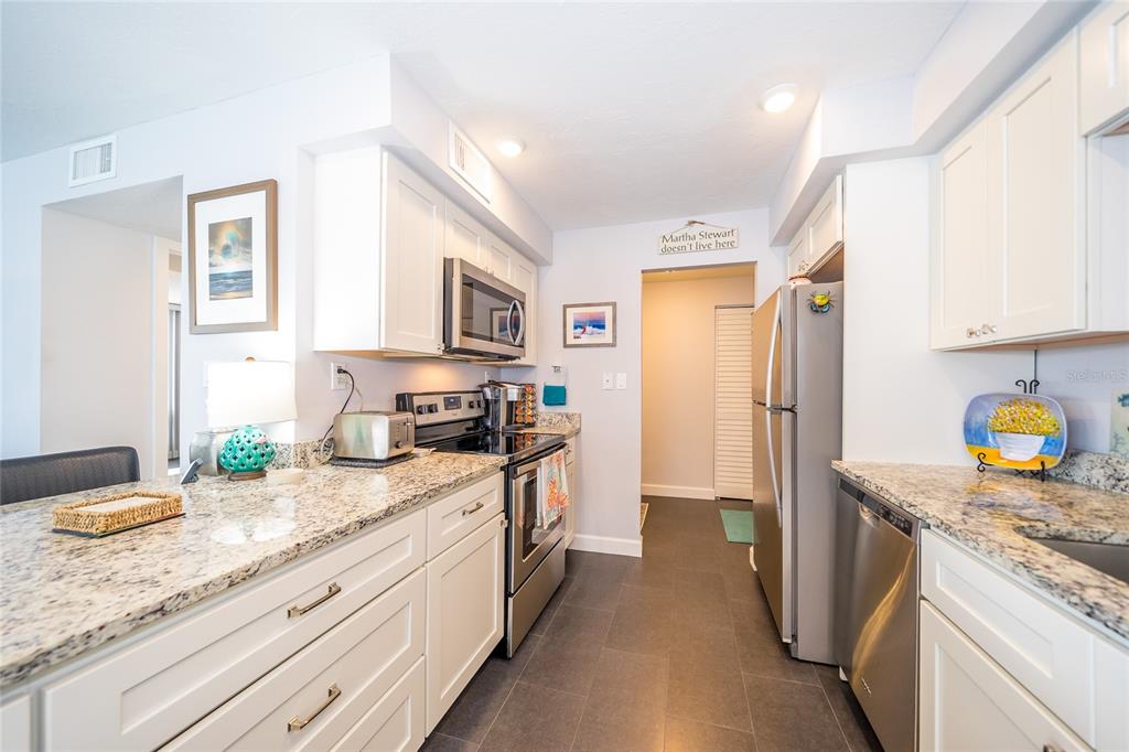 A kitchen with white cabinets, granite countertops, stainless steel appliances, and dark tile flooring — 707 S GULFSTREAM AVENUE UNIT 602, SARASOTA, FL