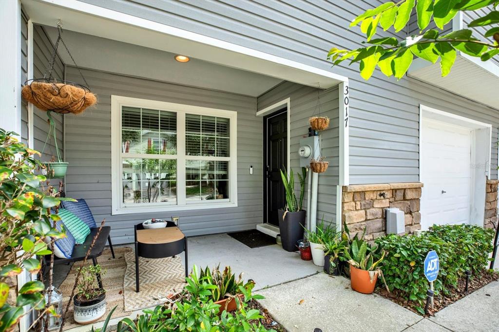 A gray-sided house exterior features a covered front porch with a bench and plants — 3017 MOJAVE OAK DRIVE, VALRICO, FL