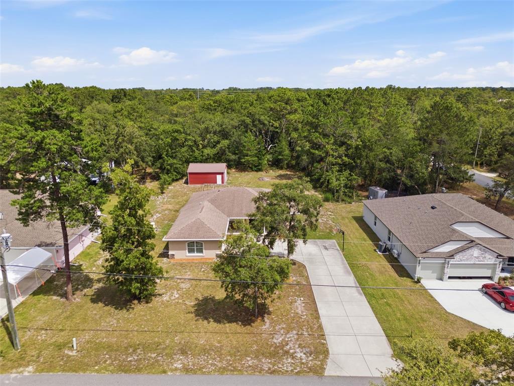 An aerial view shows a single-story house with a concrete driveway and a detached shed — 11472 PINE WARBLER AVENUE, BROOKSVILLE, FL