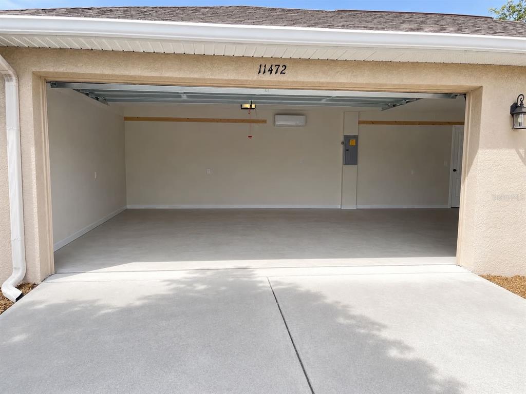 An open garage with a concrete floor, light-colored walls, and a mini-split air conditioning unit — 11472 PINE WARBLER AVENUE, BROOKSVILLE, FL