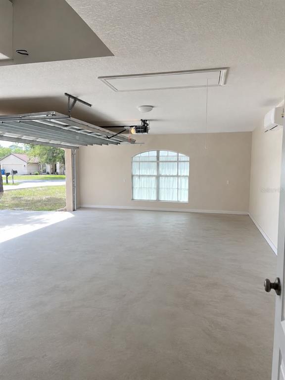 A spacious garage with a concrete floor, an open overhead door, and an arched window — 11472 PINE WARBLER AVENUE, BROOKSVILLE, FL