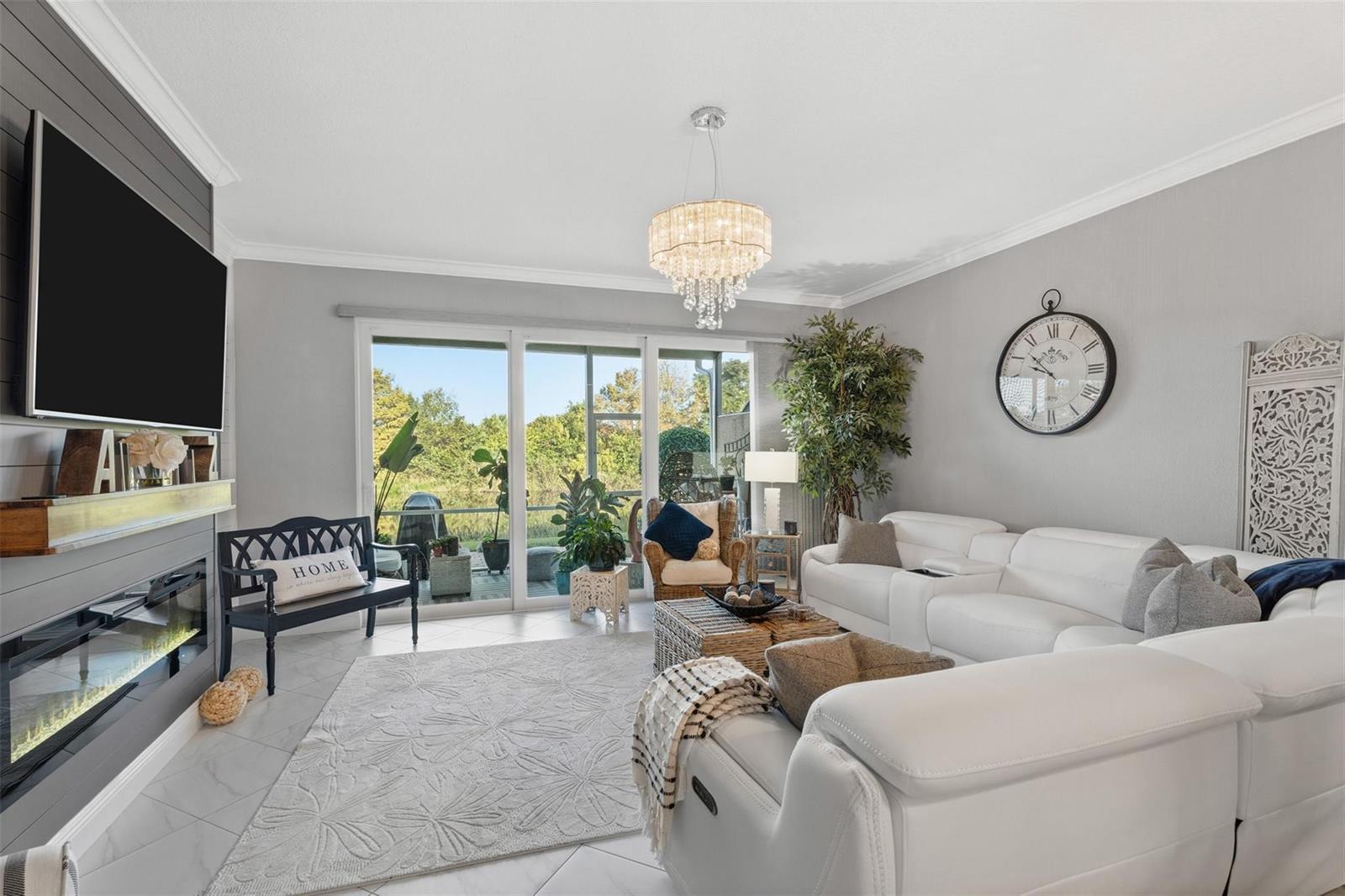 A living room features a white sectional sofa, fireplace, chandelier, and sliding glass patio doors — 651 SW Glen Crest Way # 2, Stuart FL 34997, STUART, FL