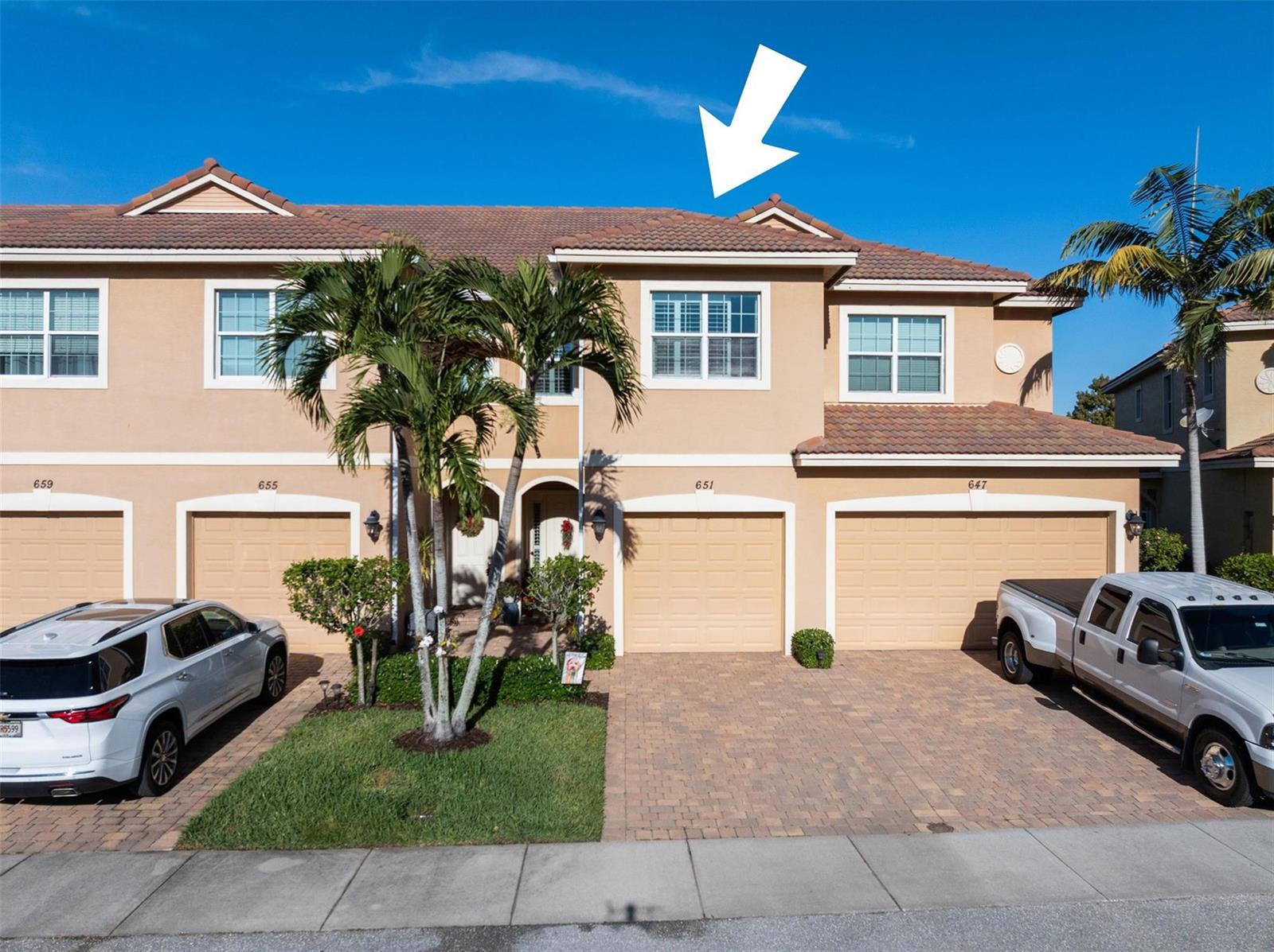 The exterior of a multi-unit residential building features tan stucco walls, tiled roofs, and garages — 651 SW Glen Crest Way # 2, Stuart FL 34997, STUART, FL