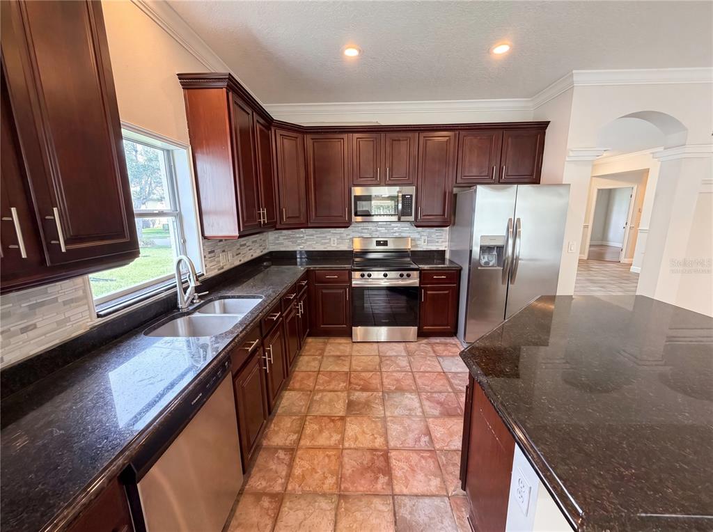 A kitchen features dark wood cabinets, granite countertops, stainless steel appliances, and tiled flooring — 3379 MORELYN CREST CIRCLE, ORLANDO, FL
