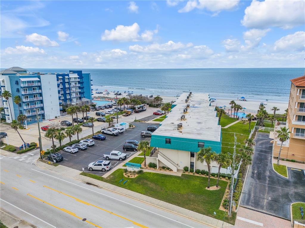 An aerial view shows a multi-story beachside apartment complex with a parking lot and ocean — 701 S ATLANTIC AVENUE UNIT UT10, NEW SMYRNA BEACH, FL