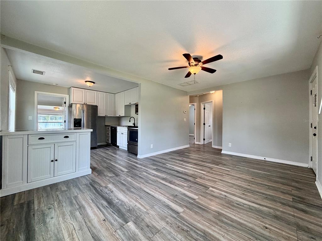 An open-concept living area features wood-look flooring, a ceiling fan, and an adjacent white kitchen — 4727 20TH STREET N, ST PETERSBURG, FL