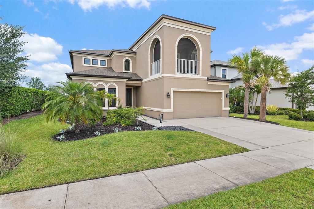 A two-story tan stucco house features a two-car garage and a second-story arched balcony — 9085 LUNA LANE, SARASOTA, FL