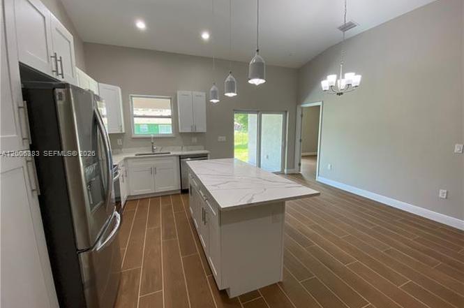A modern kitchen features white cabinets, a marble-topped island, and wood-look tile flooring — 117-119 Meadow, Lehigh Acres FL 33973, LEHIGH ACRES, FL
