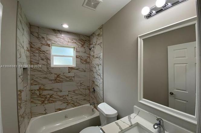 A bathroom features a tub with marble-patterned tile walls, a white vanity, and a mirror — 117-119 Meadow, Lehigh Acres FL 33973, LEHIGH ACRES, FL