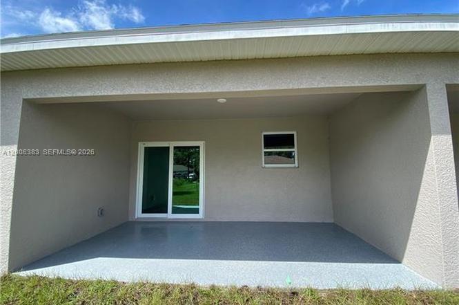 A covered concrete patio features a sliding glass door and a small window — 117-119 Meadow, Lehigh Acres FL 33973, LEHIGH ACRES, FL