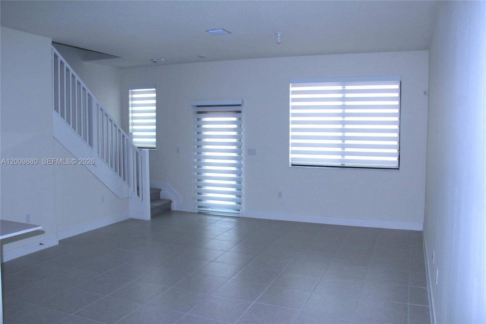 An empty room features light-colored tile flooring, a white staircase, and windows with blinds — 4272 NW 82nd Ave # 4272, Doral FL 33166, DORAL, FL