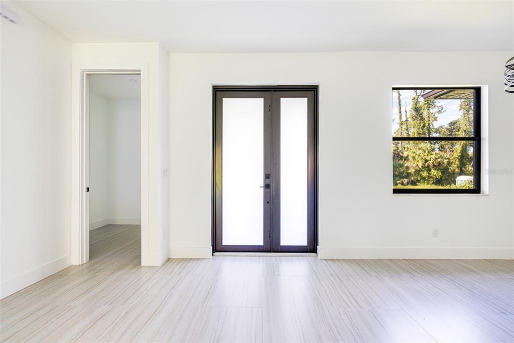 A bright room features white walls, light-colored wood-look flooring, a doorway, and double glass doors — 17196 GLENVIEW AVENUE, PORT CHARLOTTE, FL