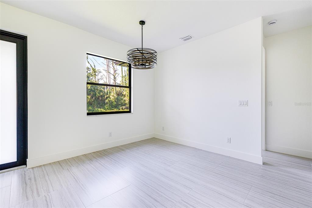 A minimalist dining room features white walls, light-colored tile flooring, and a modern metal chandelier — 17196 GLENVIEW AVENUE, PORT CHARLOTTE, FL