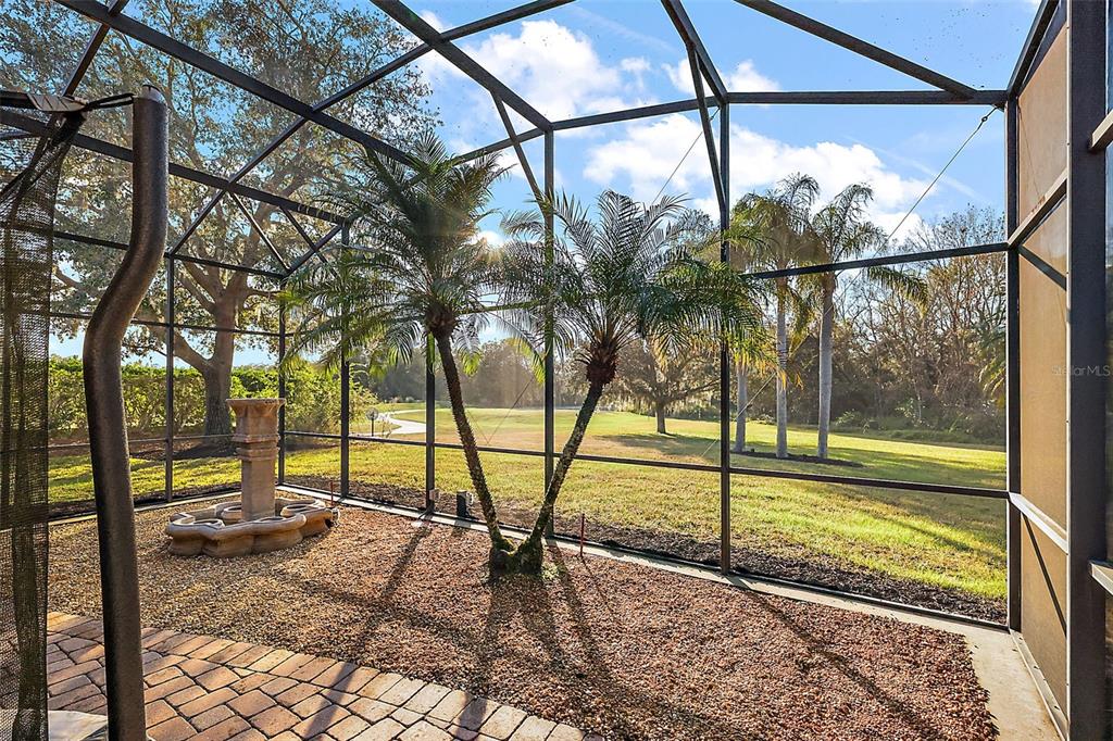 A screened-in patio features a stone fountain, two small palm trees, and gravel flooring — 9930 SANTA BARBARA COURT, HOWEY IN THE HILLS, FL