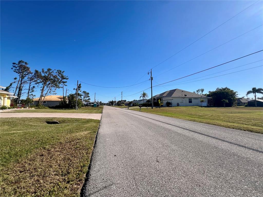 A paved residential street stretches between grassy lots with houses and utility poles — 84 FAIRWAY ROAD, ROTONDA WEST, FL