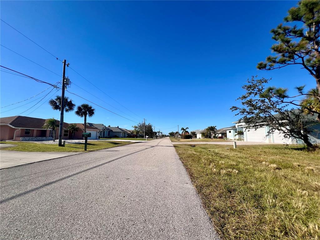 A paved residential street lined with single-story houses, palm trees, and utility poles under clear skies — 84 FAIRWAY ROAD, ROTONDA WEST, FL