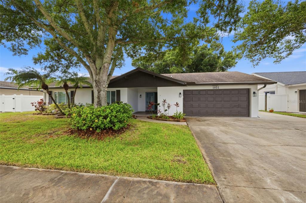 A single-story house with a white exterior, brown garage door, and a large front tree — 1931 ARVIS CIRCLE E, CLEARWATER, FL
