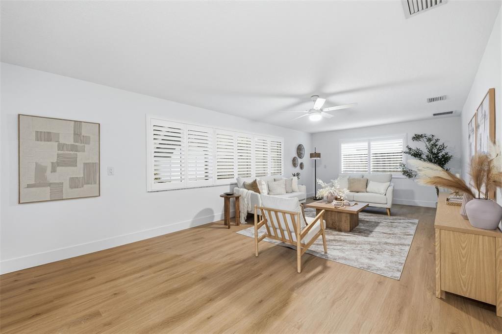 A bright living room features light wood flooring, white walls, plantation shutters, and neutral furniture — 1931 ARVIS CIRCLE E, CLEARWATER, FL