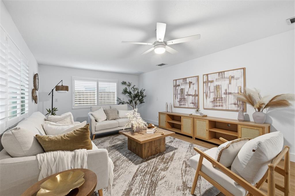 A bright living room features a white sofa, two armchairs, a wooden coffee table, and media console — 1931 ARVIS CIRCLE E, CLEARWATER, FL
