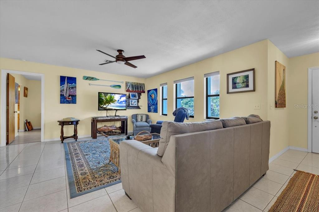 A living room with light yellow walls, tile flooring, a gray sofa, and a ceiling fan — 6150 AVILA STREET, ENGLEWOOD, FL