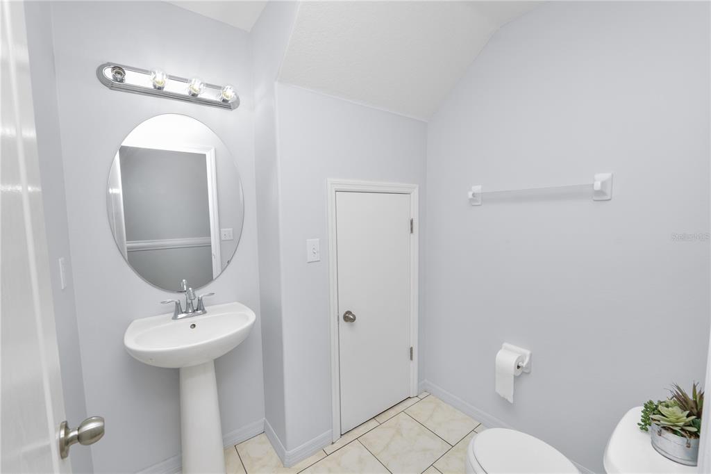 A small bathroom features a pedestal sink, a round mirror, and a white door — 5455 LIMESTONE LANE, LAKELAND, FL