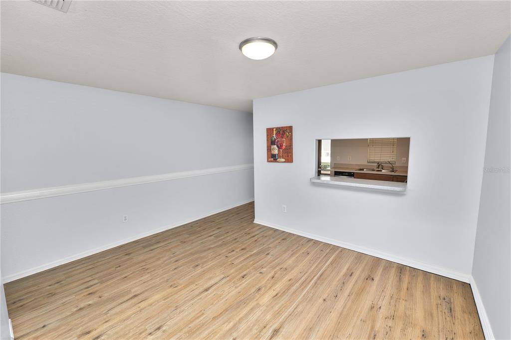 An empty dining room features light wood-look flooring, white walls, and a kitchen pass-through window — 5455 LIMESTONE LANE, LAKELAND, FL