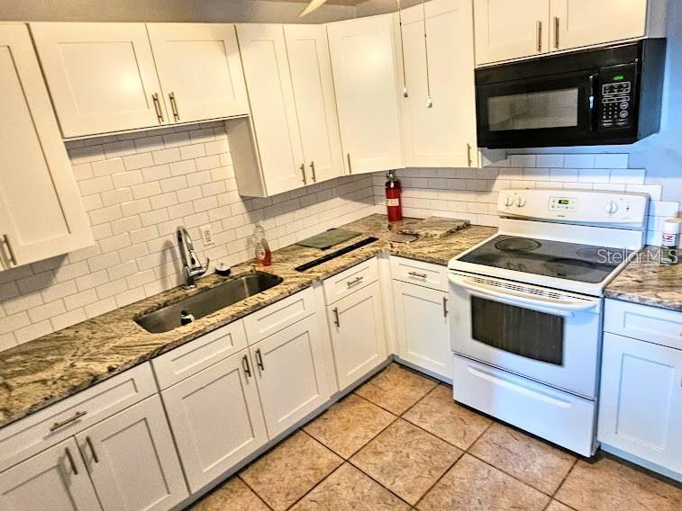 A kitchen with white cabinets, granite countertops, a subway tile backsplash, and white appliances — 6801 79TH AVENUE N, PINELLAS PARK, FL