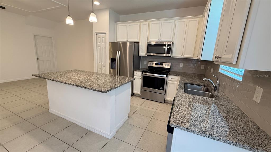 A kitchen features white cabinets, granite countertops, stainless steel appliances, and a central island — 6910 TUSSILAGO WAY, ORLANDO, FL