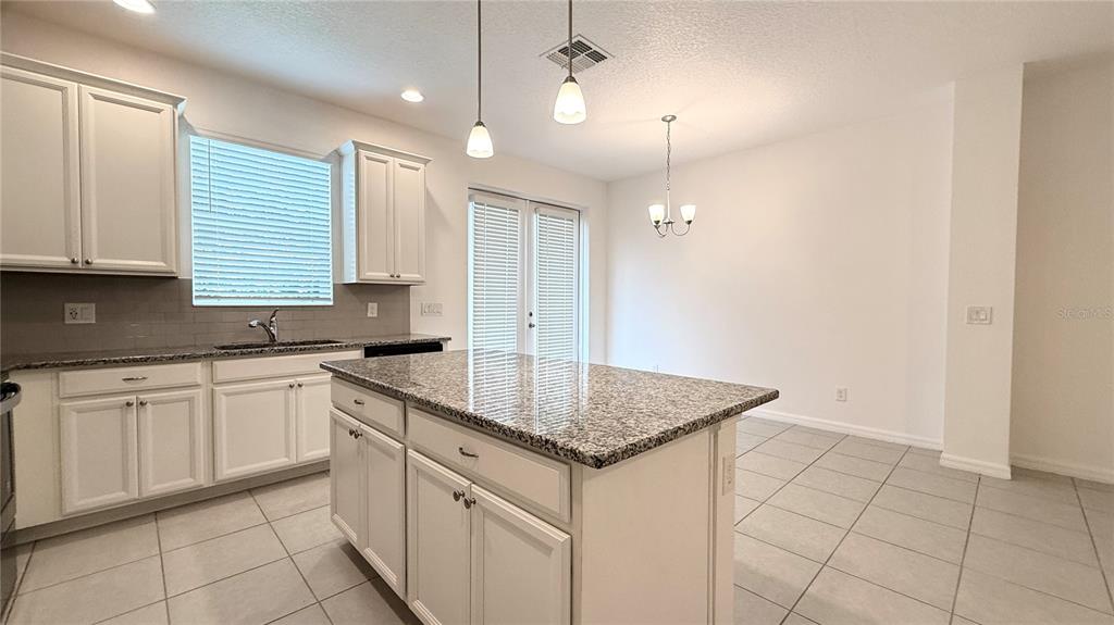 A kitchen with white cabinets, granite countertops, a center island, and a dining area — 6910 TUSSILAGO WAY, ORLANDO, FL