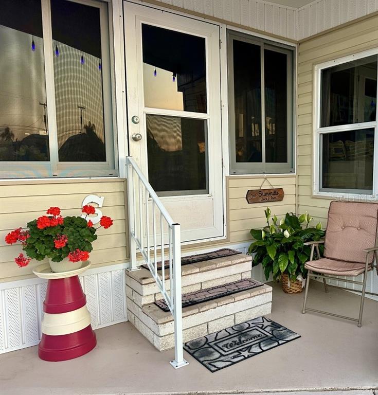 A front porch features a white door, brick steps, a potted plant, and a patio chair — 2094 DETROITER STREET, SARASOTA, FL