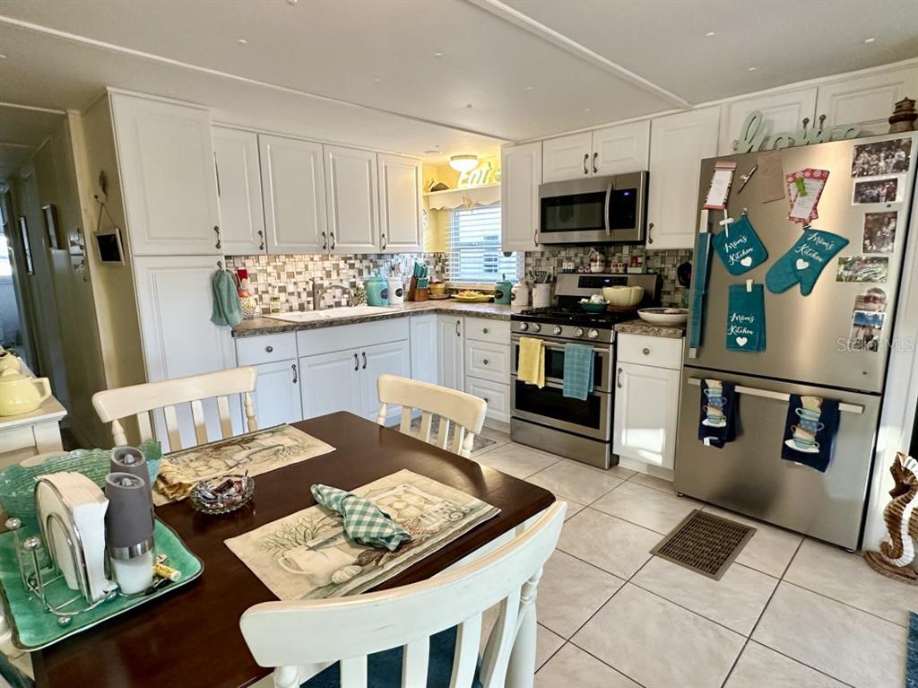 A kitchen features white cabinets, stainless steel appliances, a tiled backsplash, and a dining table — 2094 DETROITER STREET, SARASOTA, FL