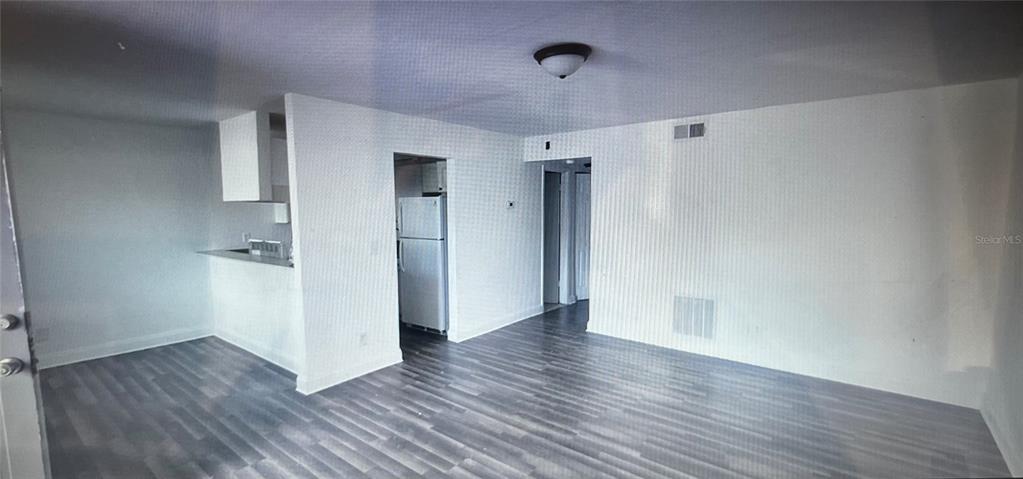An open-concept living area features light gray wood-look flooring and a kitchen with white appliances — 900 S PENINSULA DRIVE UNIT 111, DAYTONA BEACH, FL