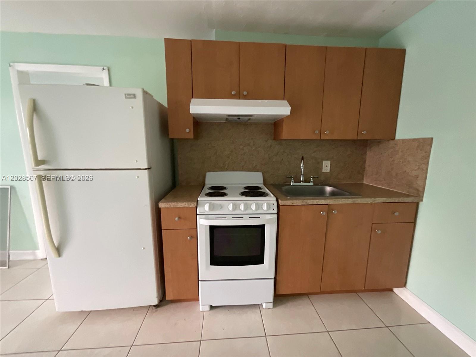 A small kitchen features light wood cabinets, a white stove, and a white refrigerator — MIAMI, FL