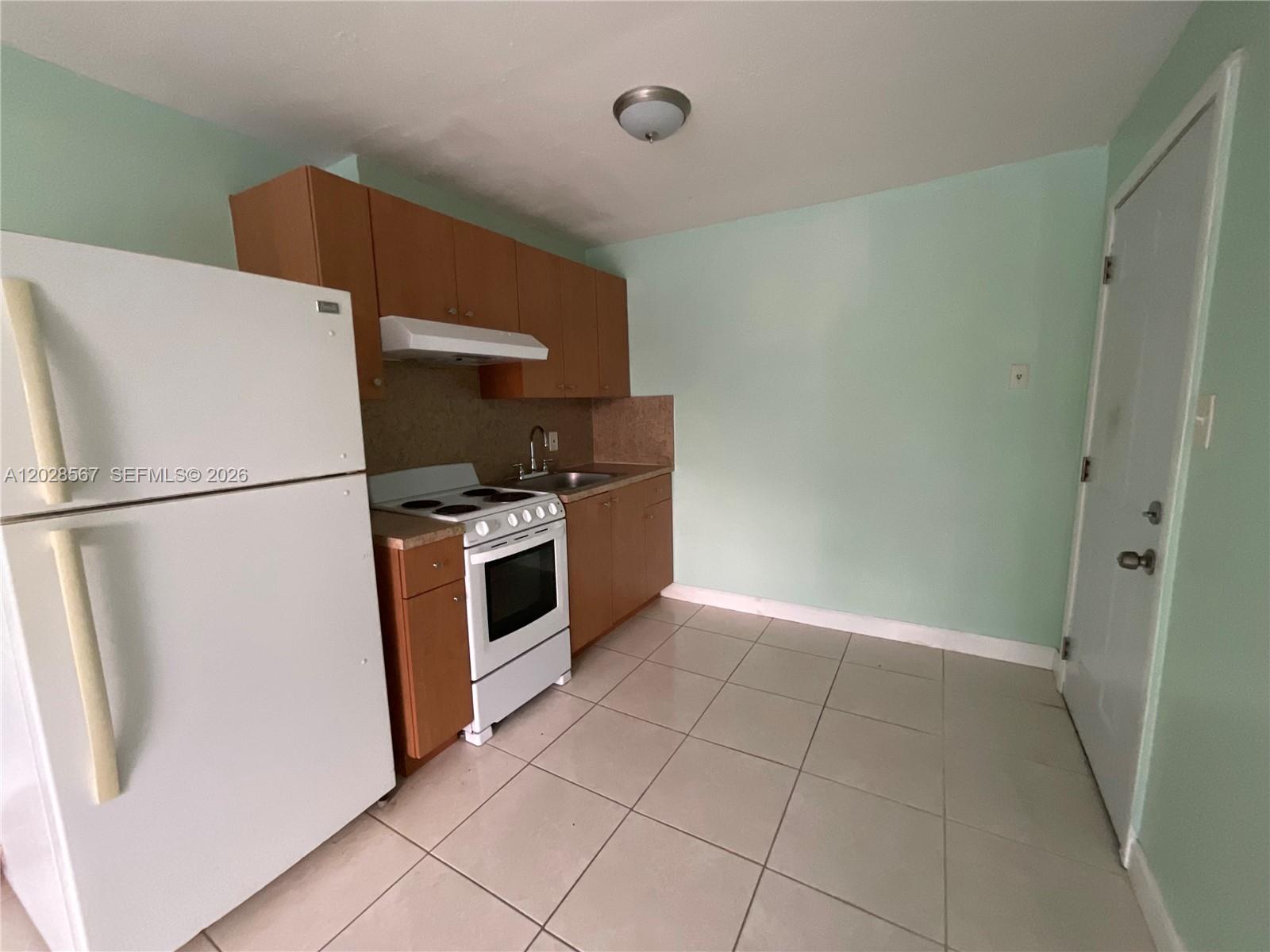 A small kitchen features light green walls, wooden cabinets, white appliances, and tiled flooring — MIAMI, FL