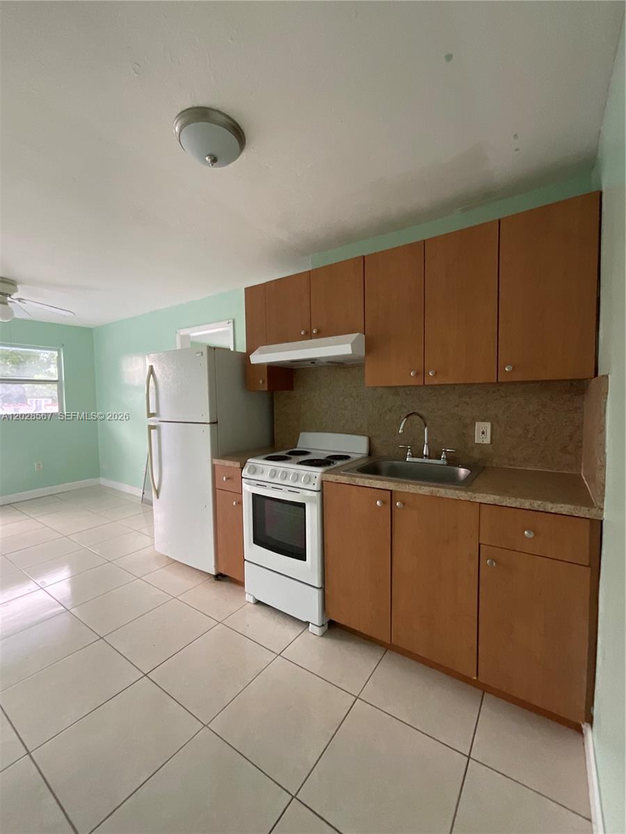 A kitchen features light wood cabinets, a white stove, a refrigerator, and light-colored tile flooring — MIAMI, FL