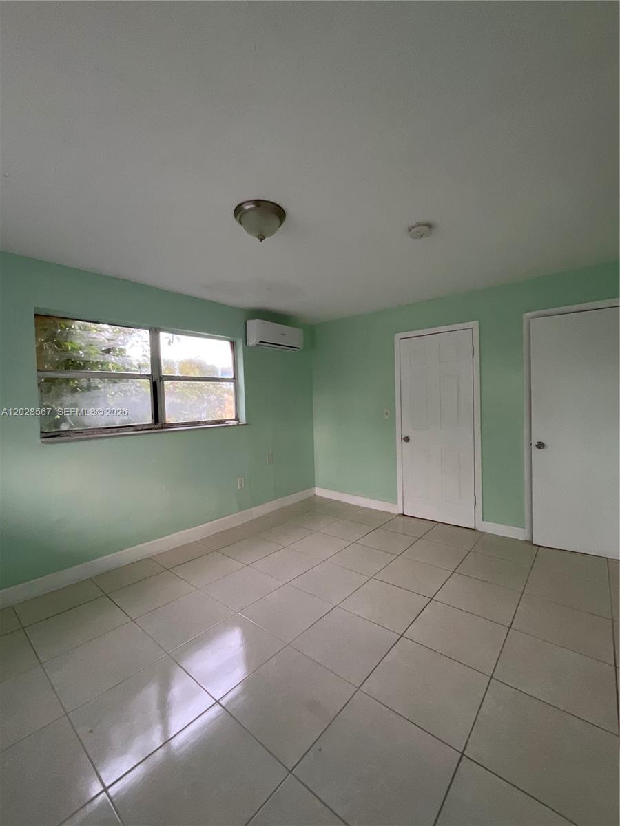 An empty room features light green walls, white tile flooring, a window, and two doors — MIAMI, FL