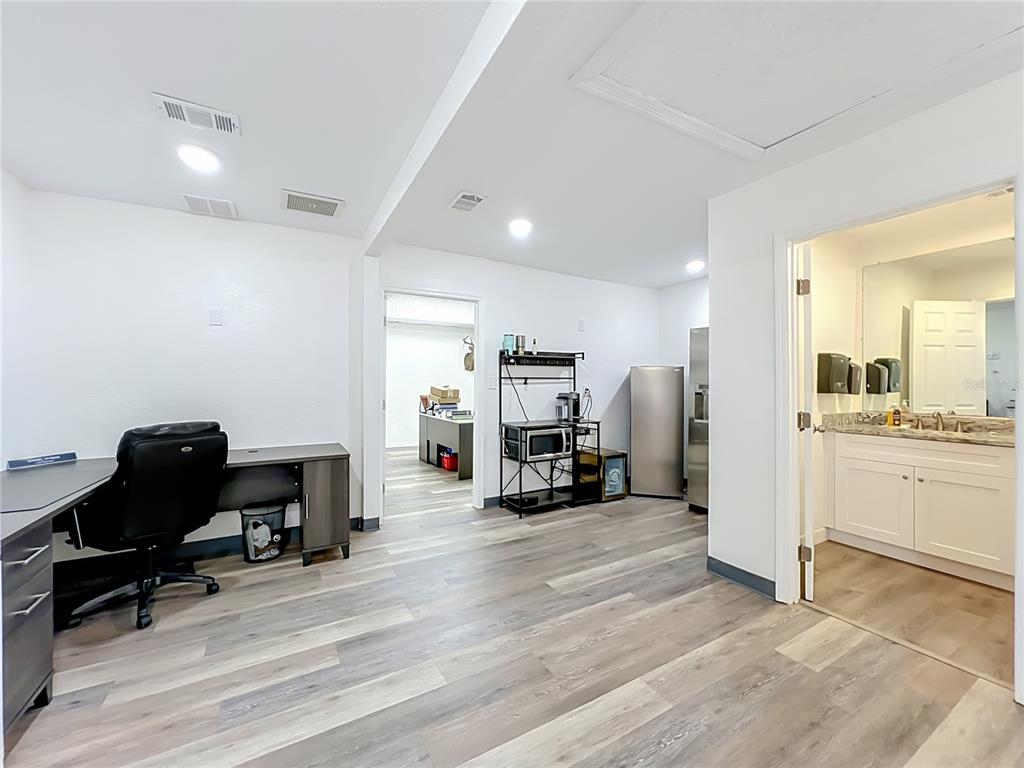 An office space with wood-look flooring, a desk, a kitchenette area, and an attached bathroom — 180 S RONALD REAGAN BOULEVARD UNIT 112, LONGWOOD, FL
