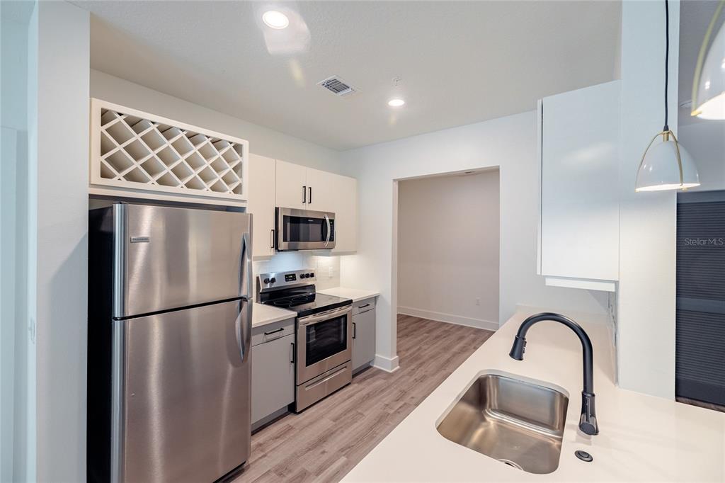 A kitchen features stainless steel appliances, white cabinetry, a wine rack, and a sink island — 1420 LAKEFRONT DRIVE UNIT 6413, SARASOTA, FL