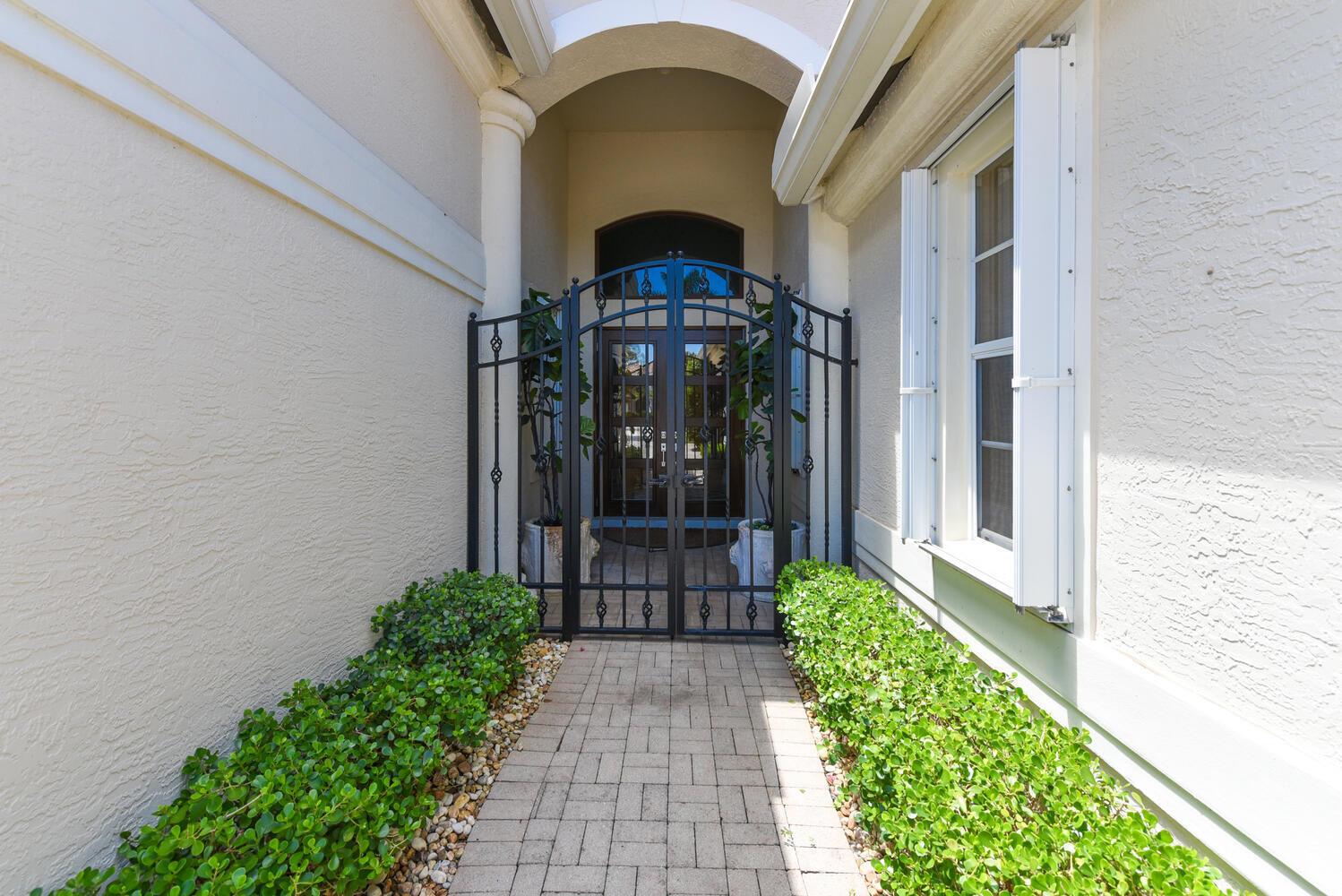 A paved walkway leads to a gated entryway with potted plants and a white exterior — 14284 Stroller Way, Wellington FL 33414, WELLINGTON, FL