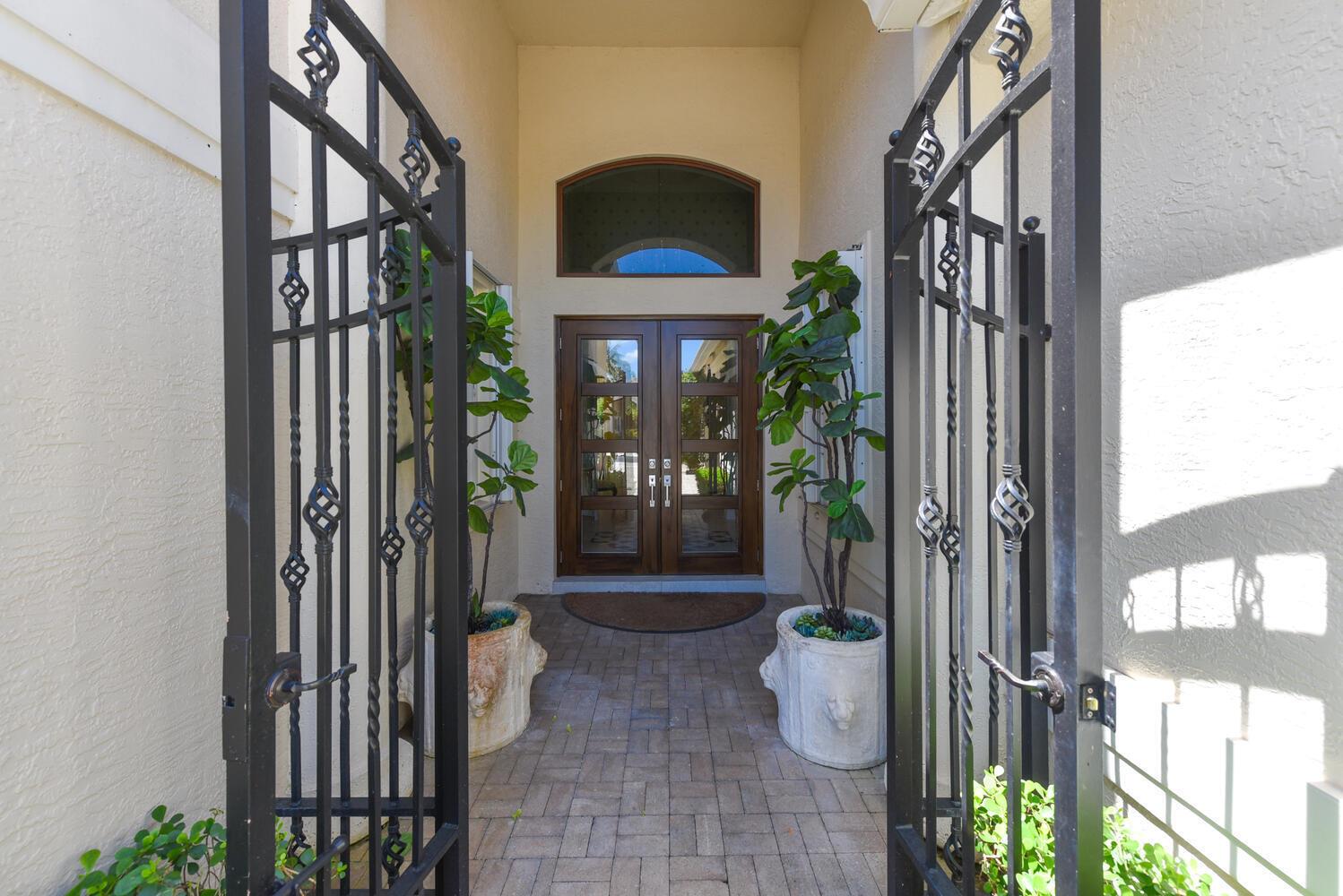A paved entryway features double wooden doors flanked by two large potted fiddle leaf figs — 14284 Stroller Way, Wellington FL 33414, WELLINGTON, FL
