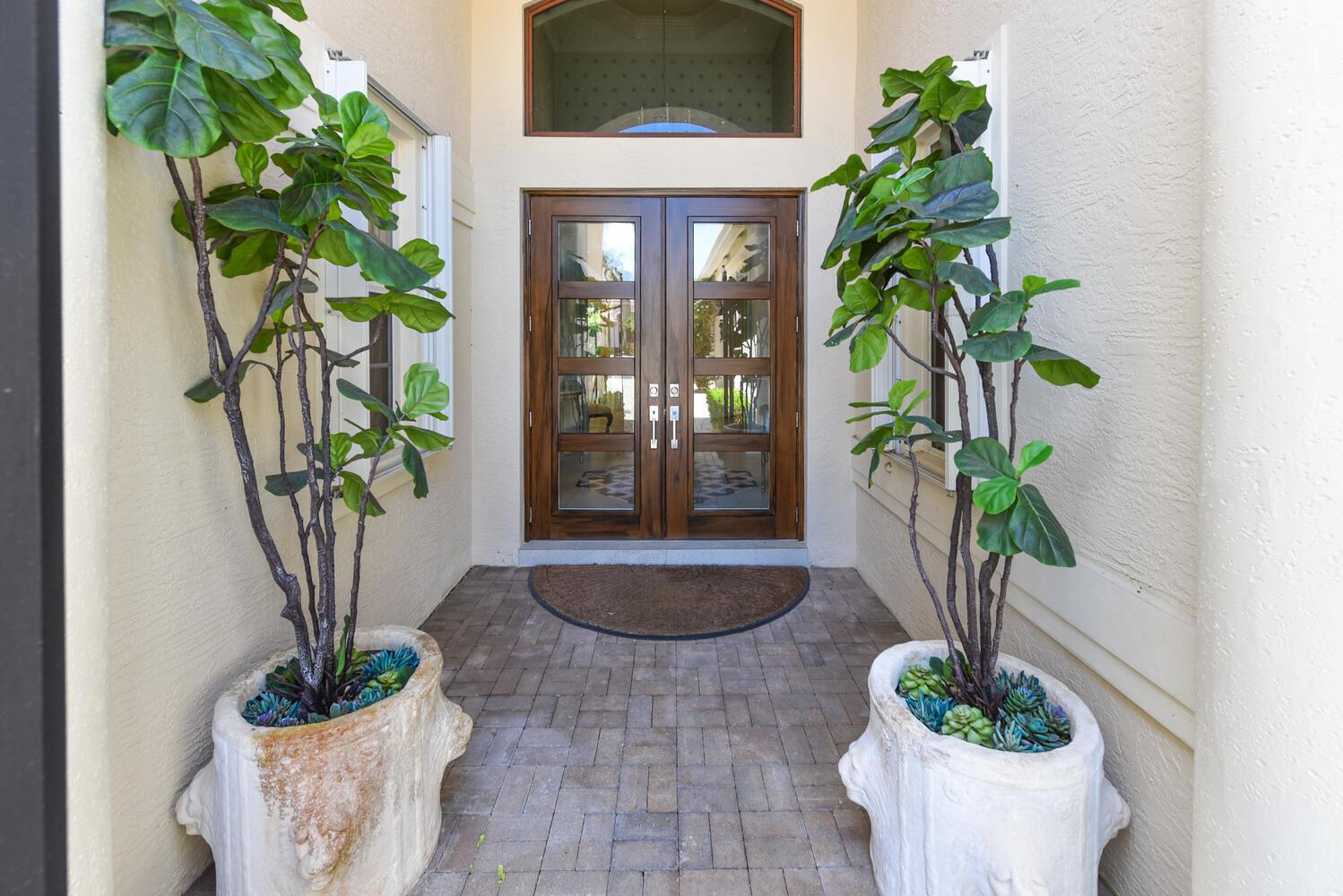 A front entryway features double wooden doors, a brick floor, and two large potted plants — 14284 Stroller Way, Wellington FL 33414, WELLINGTON, FL