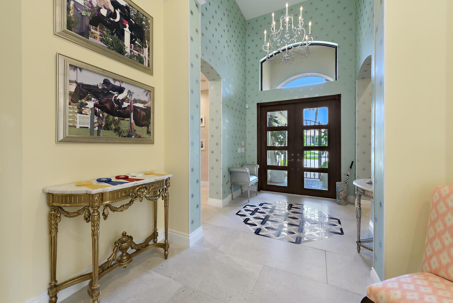 A bright foyer features a patterned accent wall, a crystal chandelier, and a marble console — 14284 Stroller Way, Wellington FL 33414, WELLINGTON, FL