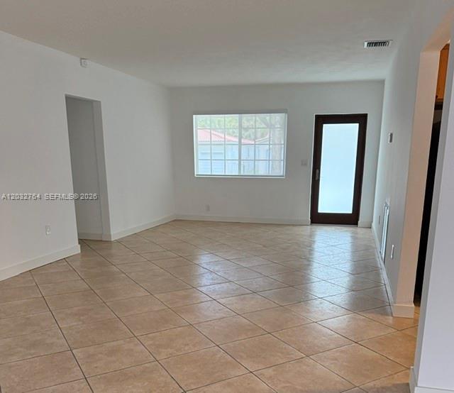 An empty room with beige tile flooring, white walls, a window, and a glass-paneled door — 753 Navarre Ave, Coral Gables FL 33134, CORAL GABLES, FL