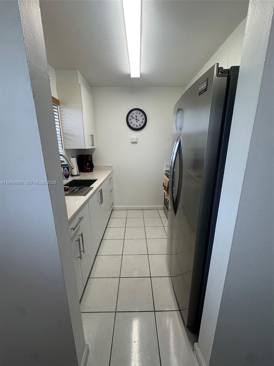 A narrow galley kitchen features white cabinets, stainless steel appliances, and white tiled floors — 13671 SW 62nd St # 1, Miami FL 33183, MIAMI, FL