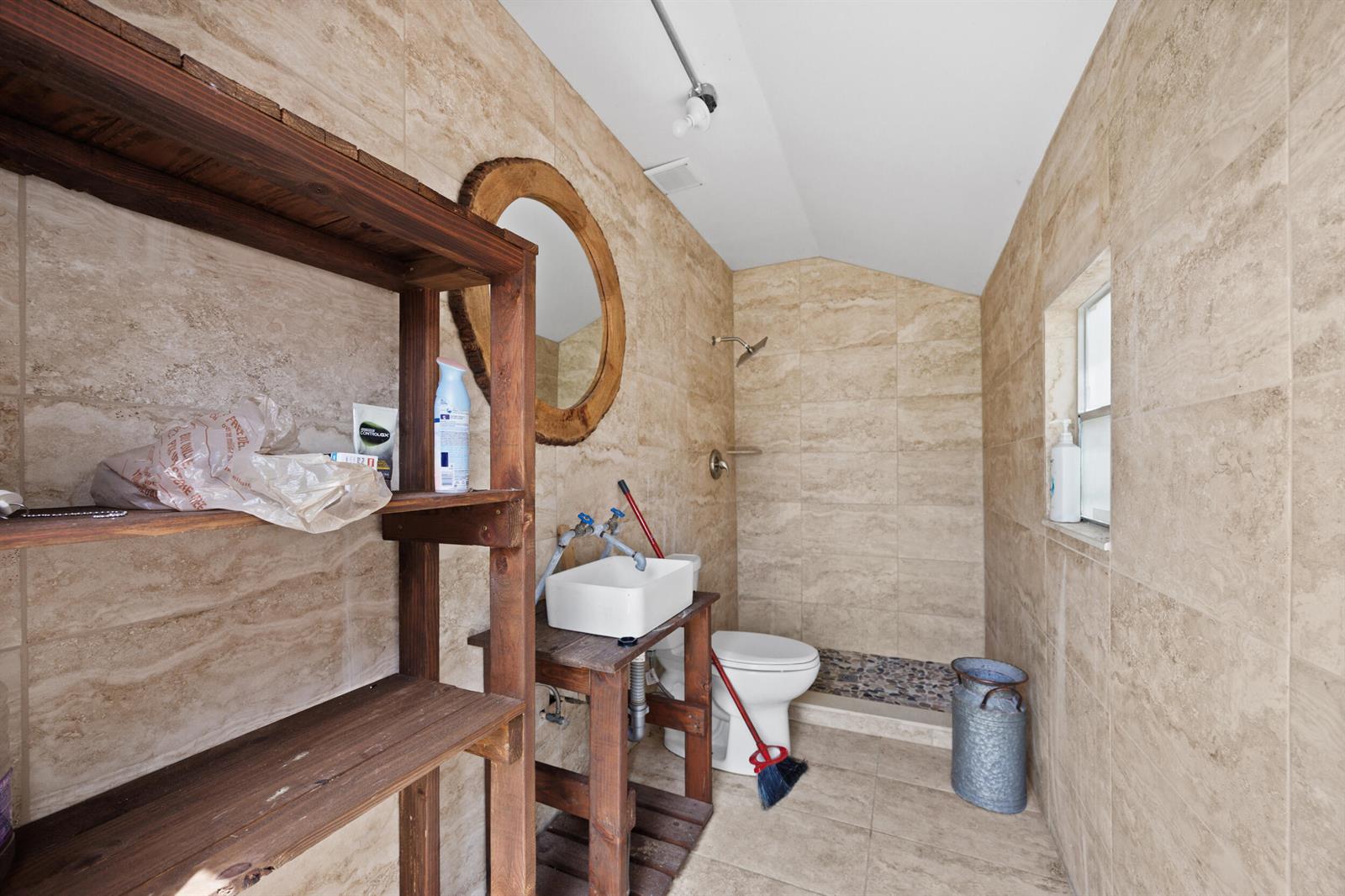 A rustic bathroom features beige tiled walls, a wooden vanity, and an open shower area — 20914 NW 280th Street, Okeechobee FL 34972, OKEECHOBEE, FL