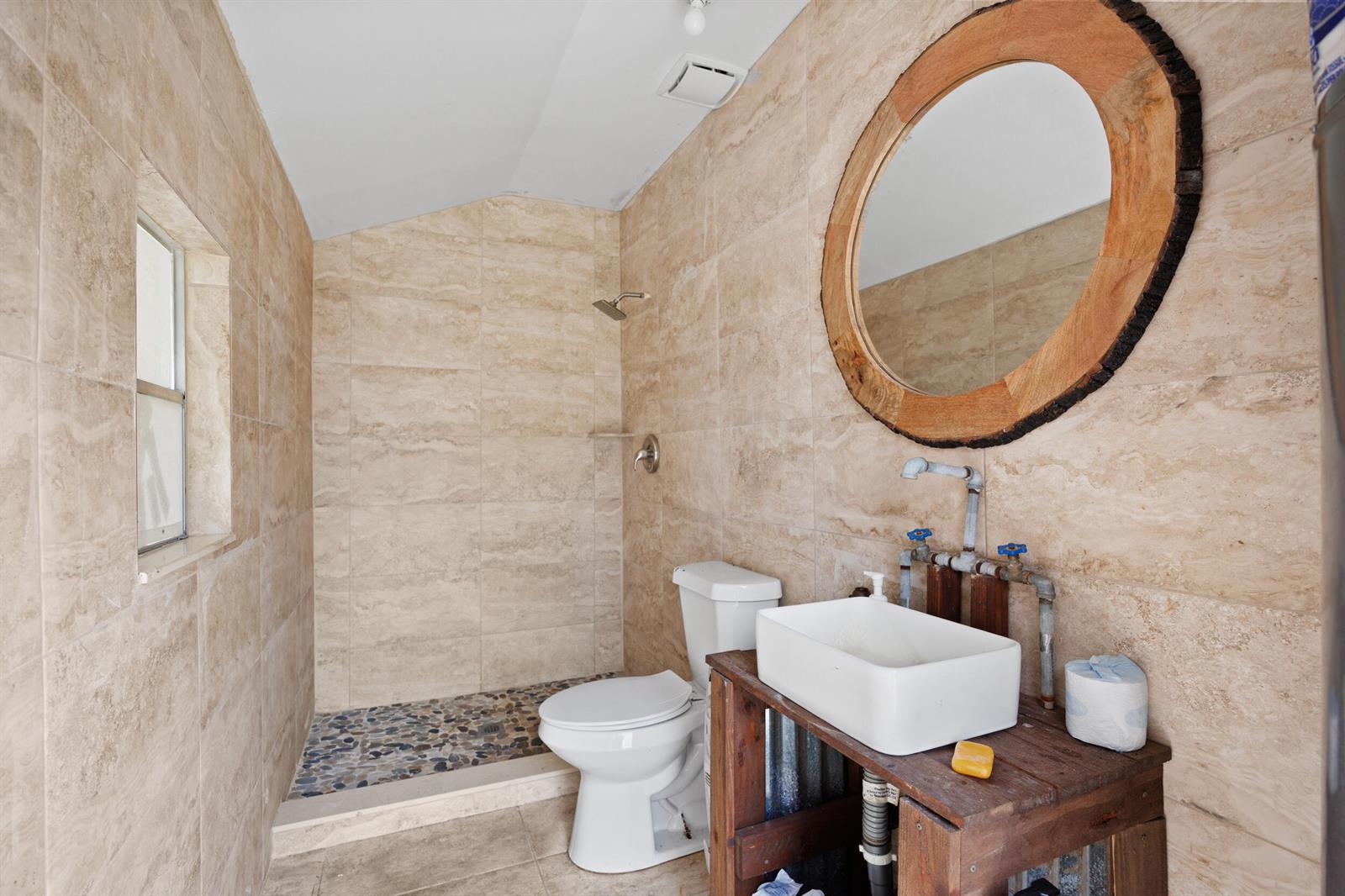 A bathroom with beige tile walls, a pebble-floor shower, a toilet, and a rustic vanity — 20914 NW 280th Street, Okeechobee FL 34972, OKEECHOBEE, FL