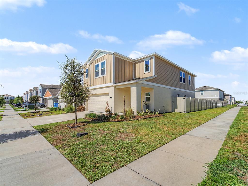 A two-story suburban house with a tan exterior, a garage, and a side privacy fence — 7587 STARFLOWER WAY, WESLEY CHAPEL, FL