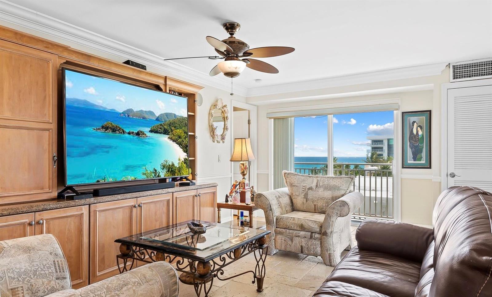 A living room features a large television, wooden cabinetry, patterned armchairs, and a balcony view — 4511 S Ocean Boulevard # 601, Highland Beach FL 33487, HIGHLAND BEACH, FL